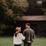 A couple walks through a grassy area towards a rustic barn, capturing a romantic autumn ambiance.